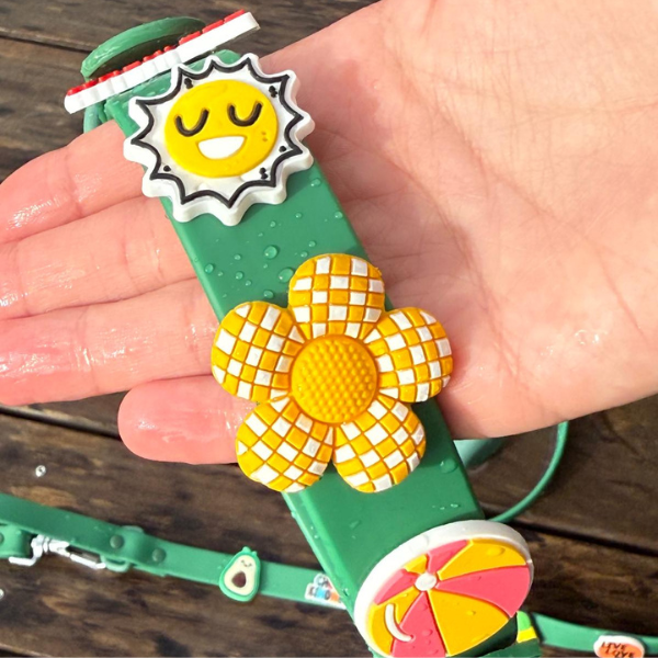 Colorful dog collar with sun and flower design held by a hand on a wooden surface